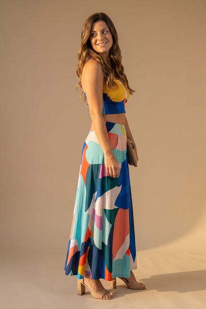 Osanna Creazione women's long, flowing skirt with a vibrant abstract print in blue, yellow, pink, and teal. Features pockets and an A-line cut.