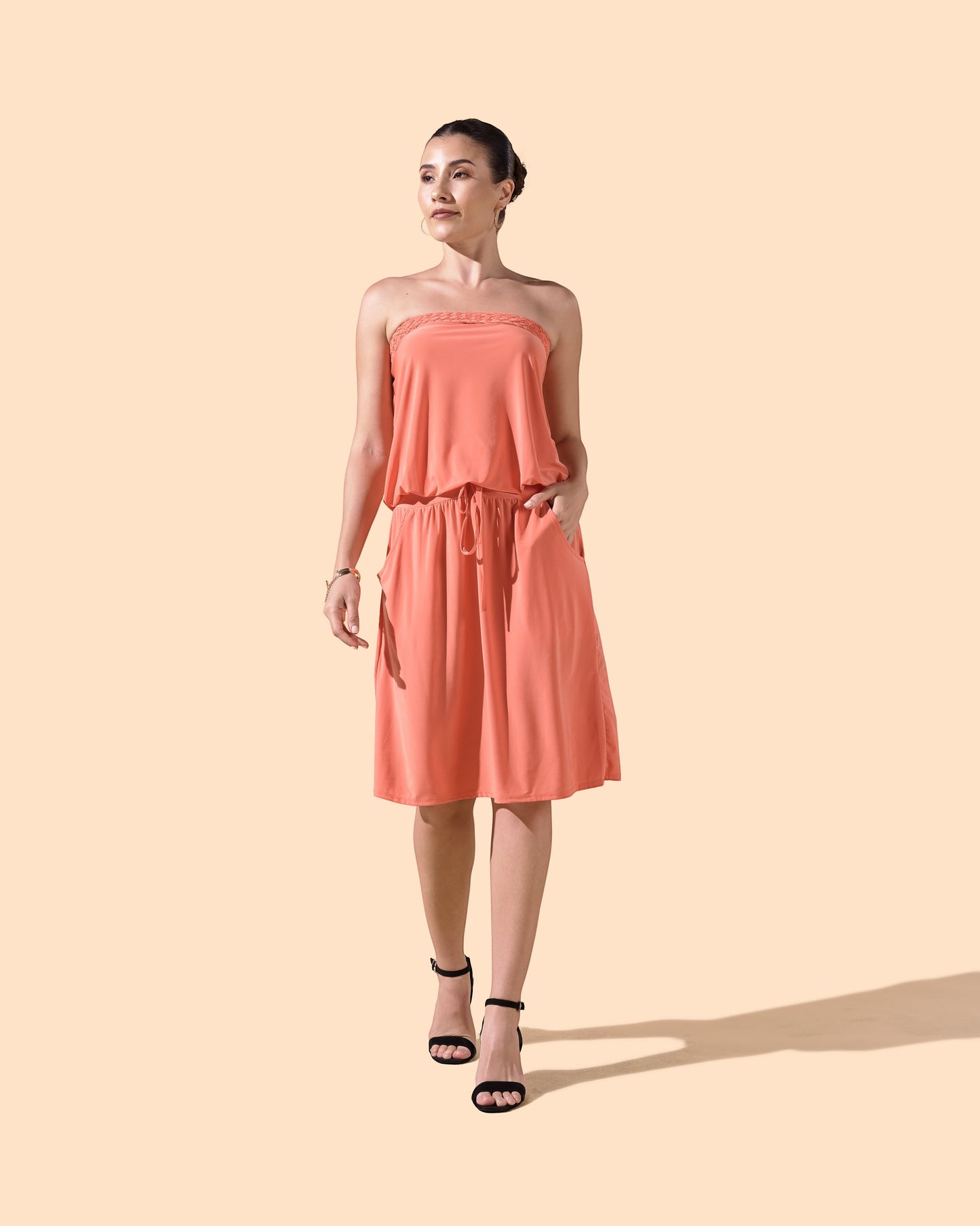 Osanna Creazione coral strapless short dress with braided bustier, blousant top, and pockets. Model is wearing black heels.
