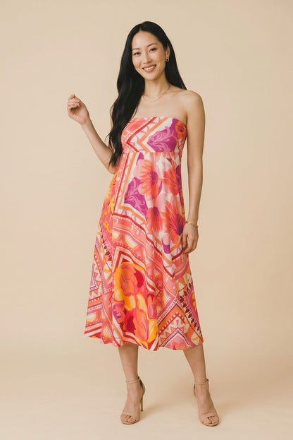 Osanna Creazione Florence strapless maxi dress in vibrant floral print with pink, orange, and purple hues. Features a bandeau top and flowing skirt.