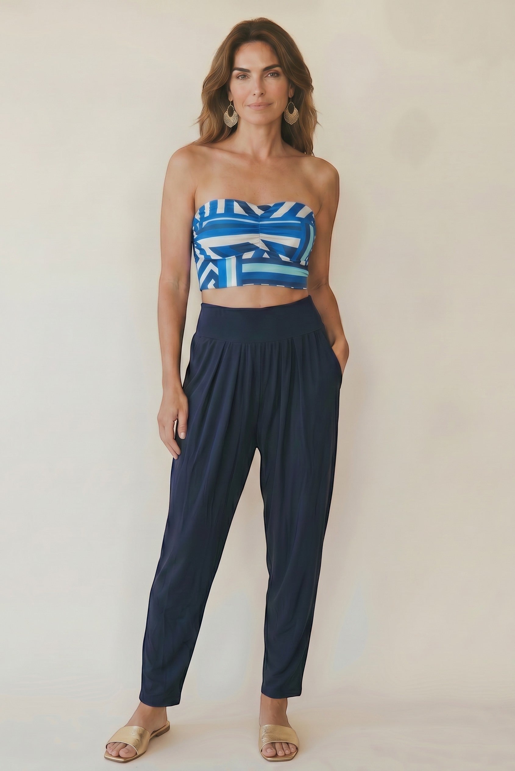 Osanna Creazione navy blue fluid tapered pants with high elasticated waist and side pockets, worn by a model with a patterned bandeau top.