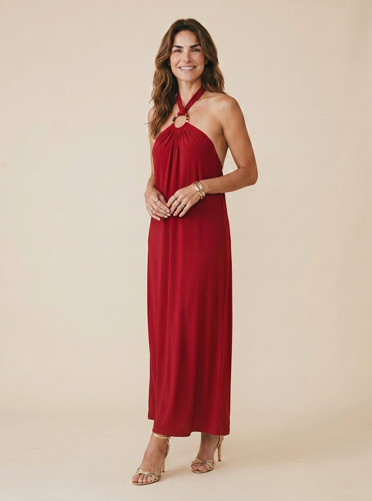 Robe longue rouge dos nu Jilo d'Osanna Creazione avec anneau doré au cou, matière fluide, portée par une femme avec sandales dorées.