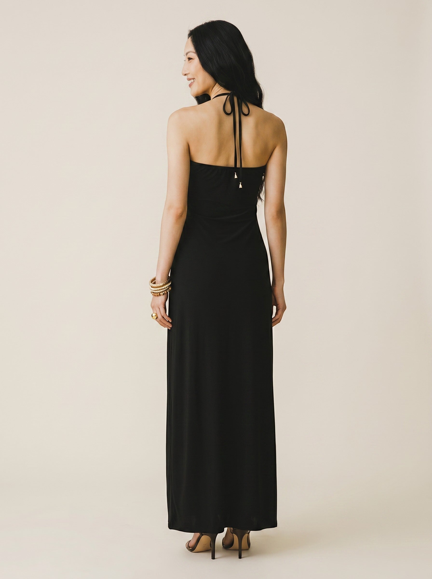 Osanna Creazione robe longue noire dos nu avec bijou doré géométrique, fente latérale et découpe au ventre. Matière fluide.
