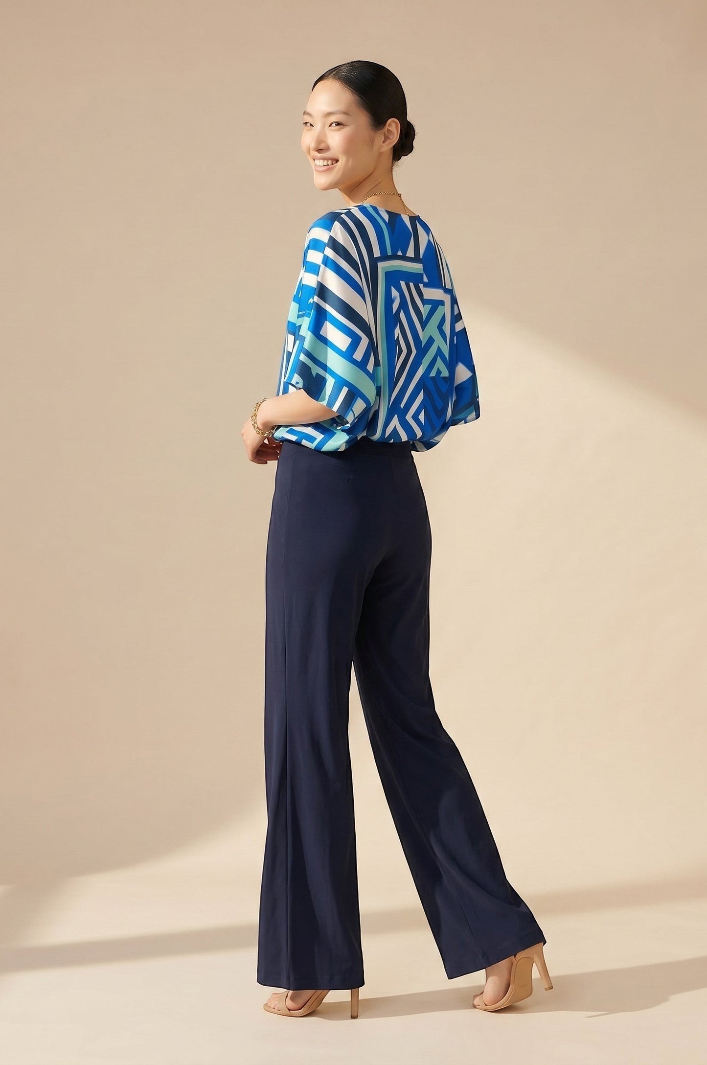 Top fluide col V bleu et blanc à motif géométrique, manches larges, coupe ample. Pantalon bleu marine taille haute. Osanna Creazione.